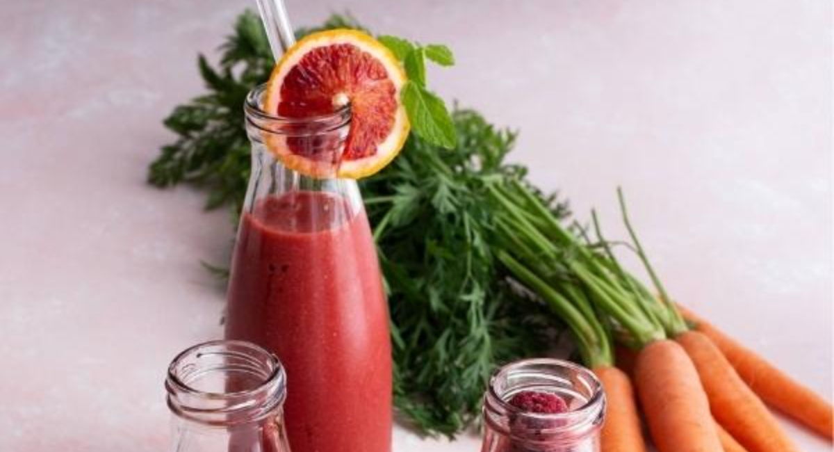 A vibrant pink smoothie topped with fresh strawberries, raspberries, chia seeds, and mint leaves in a clear glass, promoting healthy skin and natural glow.