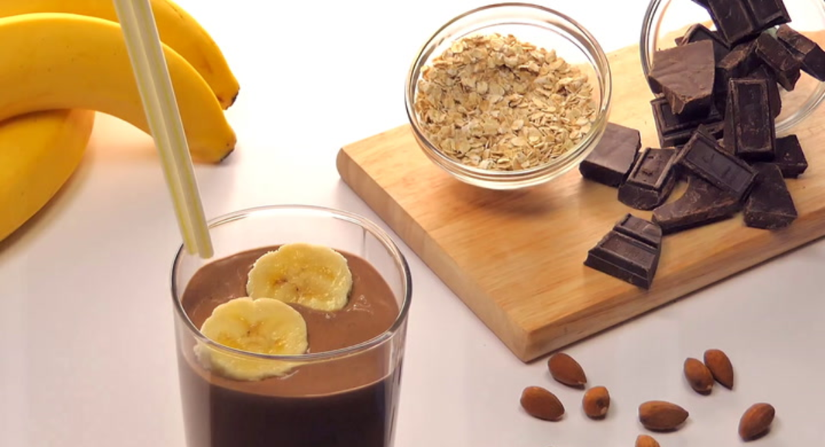 Glass of homemade chocolate banana smoothie prepared with banana, cocoa powder, peanut butter, and milk, topped with banana slices and cocoa powder.