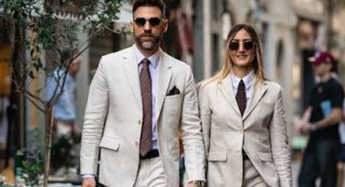 A stylish woman wearing timeless wardrobe essentials including a white button-down shirt, blue jeans, tailored blazer, trench coat, little black dress, white sneakers, and classic loafers.