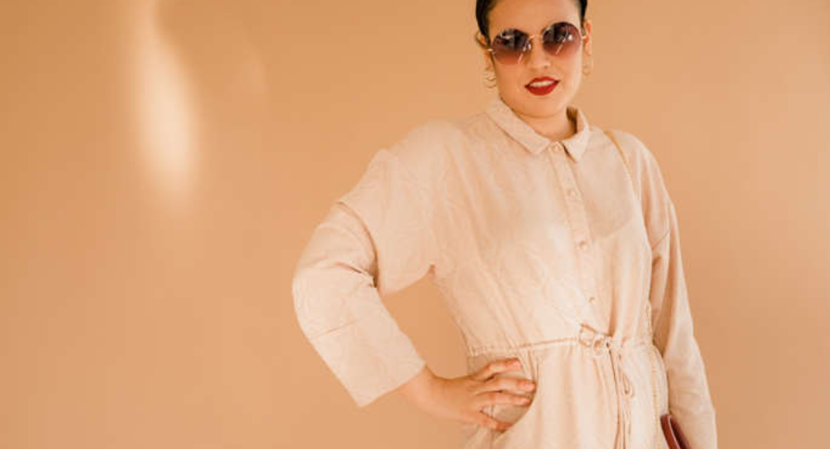 A neatly organized minimalist wardrobe featuring a white button-down shirt, neutral sweater, tailored blazer, blue jeans, little black dress, white sneakers, ankle boots, and timeless accessories in soft neutral tones.