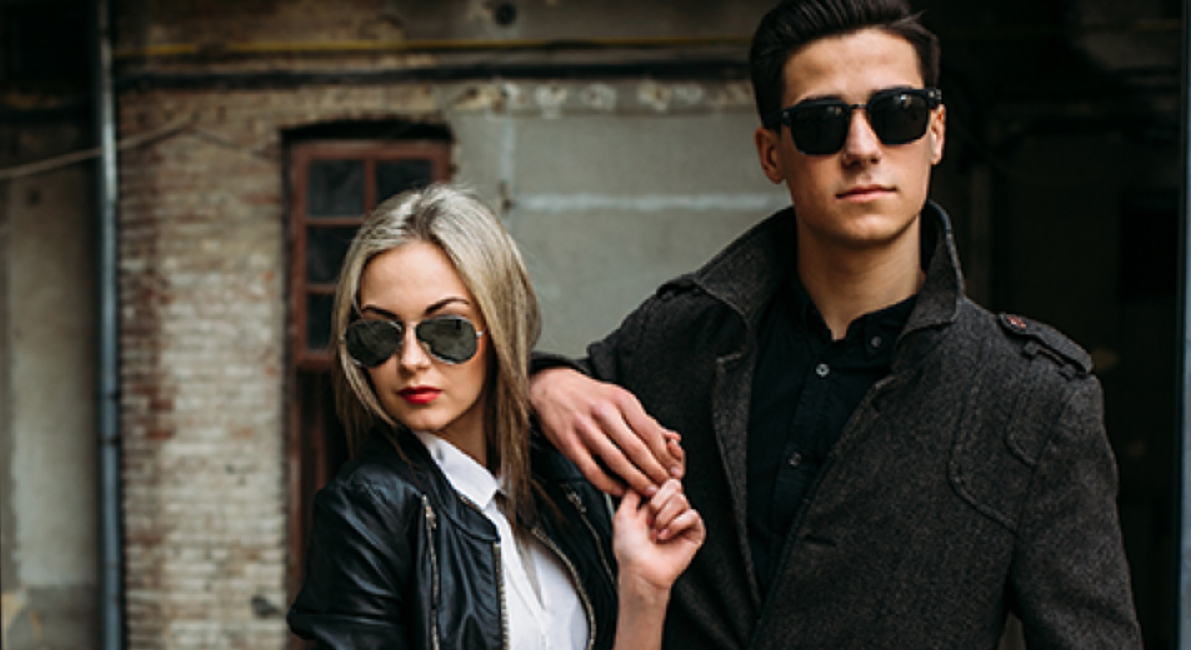 A curated collection of timeless fashion essentials including a tailored blazer, white button-down shirt, trench coat, blue jeans, little black dress, white sneakers, leather loafers, and a structured handbag in neutral tones.